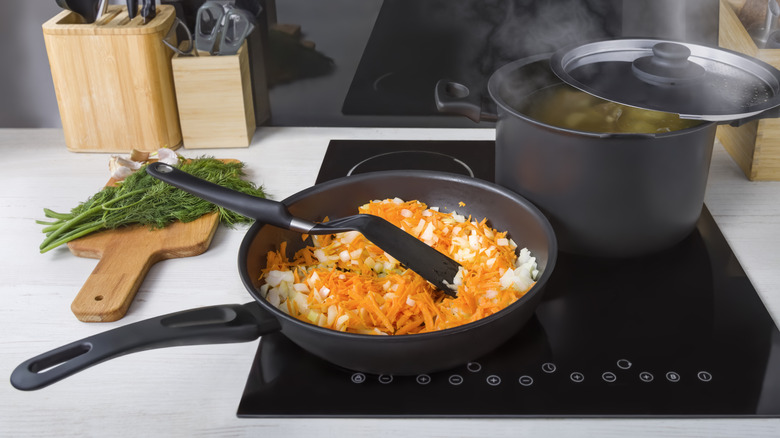 Making dinner on an induction stovetop with a pot and pan full of food.