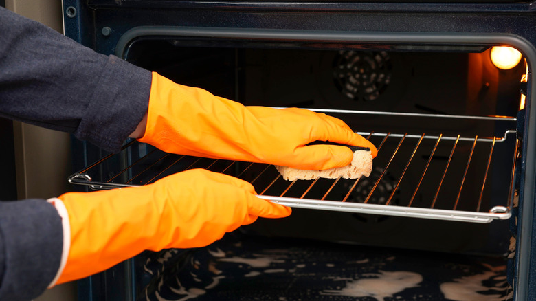 Gloved hands cleaning oven rack in open oven.
