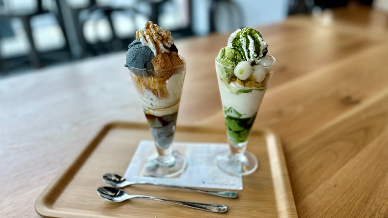 Two ice cream parfaits with spoons on wooden tray inside restaurant.