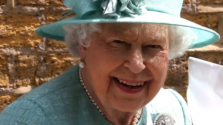  królowa elżbieta ii z szerokim uśmiechem i turkusowym kapeluszem