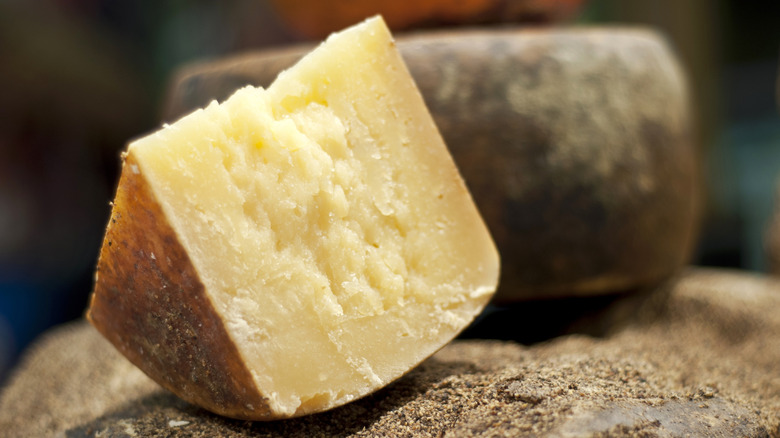 A triangular wedge of Pecorino cheese sits next to a full, uncut round of Pecorino cheese.