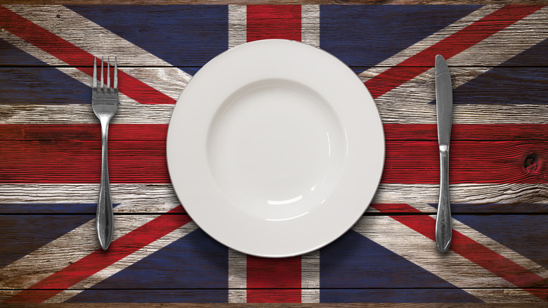 A British Union Jack painted on a wooden table with a plate over it, a knife and fork on either side.