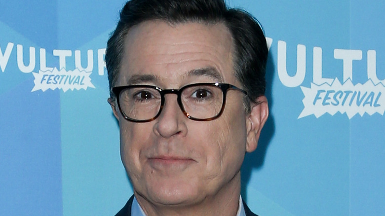 Stephen Colbert wearing glasses on blue background
