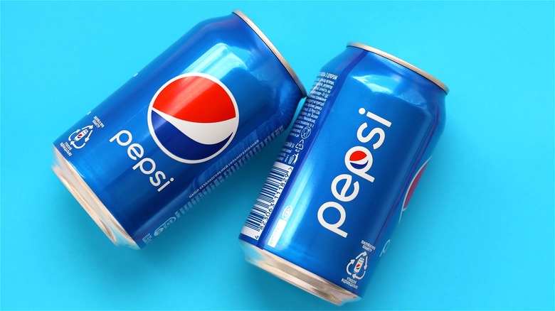 Two pepsi cans on blue back drop