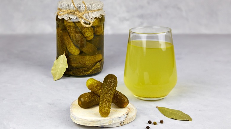 A cup of pickle brine next to a jar of pickles