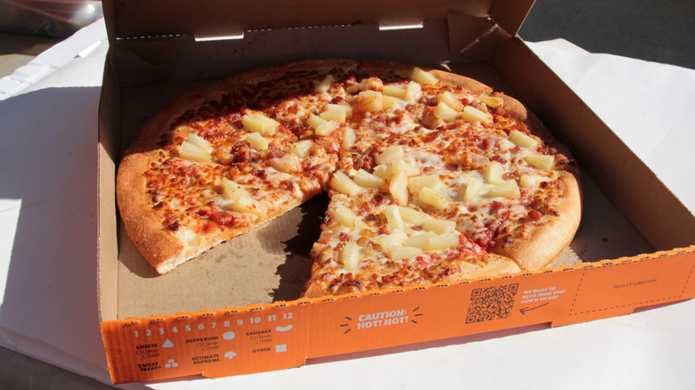 Little Caesars pineapple pizza in orange box with slice removed.