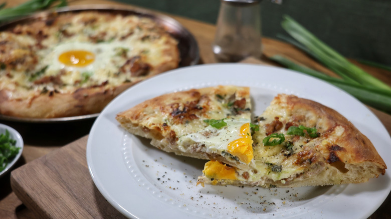 two slices of a sausage gravy breakfast pizza on a plate with a whole pizza in the background