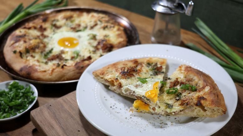 sausage gravy breakfast pizza slices on plate with whole pizza in pan behind it