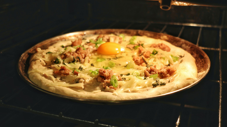 uncooked sausage gravy breakfast pizza on pan in oven