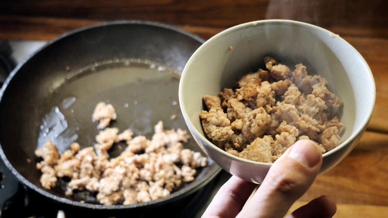 hand holding steaming bowl of crumbled breakfast sausage next to skillet of susage