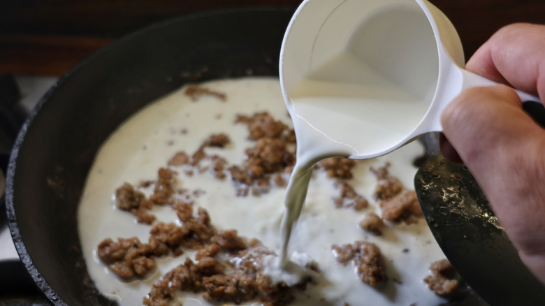 milk pouring from measuring cup into skillet of crumbled sausage