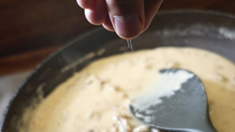fingers sprinkling salt into a skillet of sausage gravy