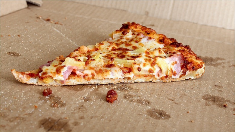 A slice of Hawaiian pizza in a cardboard pizza box