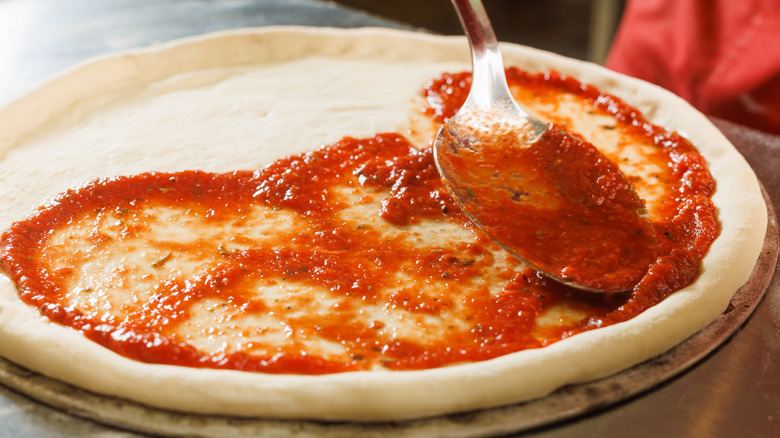 A rich red pizza sauce is being spread over pizza dough.