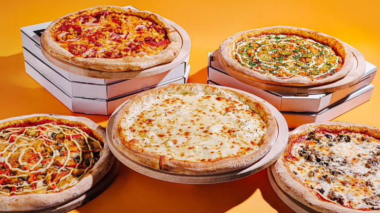 Various pizzas and boxes on yellow surface