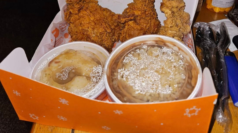 A Popeyes takeout box with bone in chicken, tenders, mashed potatoes with gravy, and red beans with rice