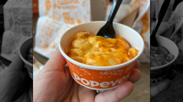 A hand holding up a regular Popeyes mac & cheese