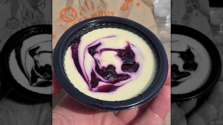 A hand holds up a Popeyes blueberry lemon cheesecake cup