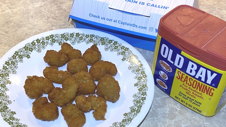 Captain D's Old Bay popcorn shrimp on plate next to takeout box and Old Bay spice jar