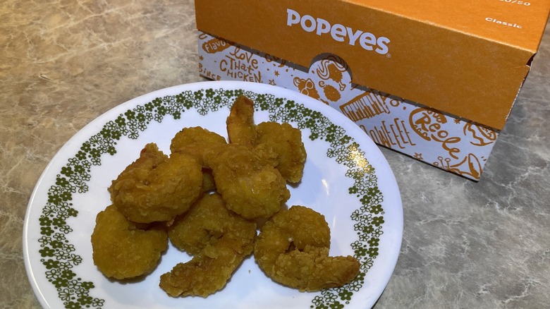 Popeyes popcorn shrimp on plate next to takeout box
