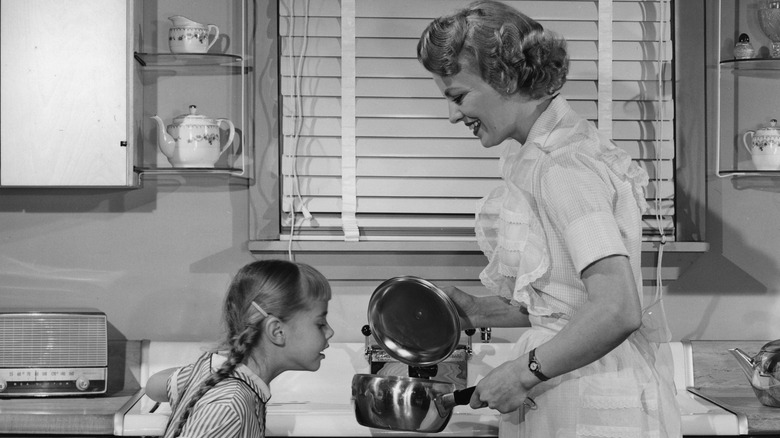 Mom and daughter in '50s kitchen with a pot of food