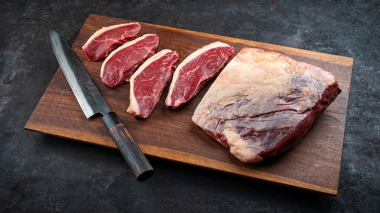 Raw aged picanha sliced into individual steaks on a wooden board