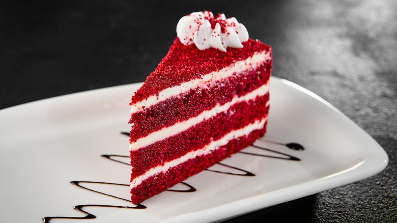 slice of red velvet cake on white plate with chocolate drizzle