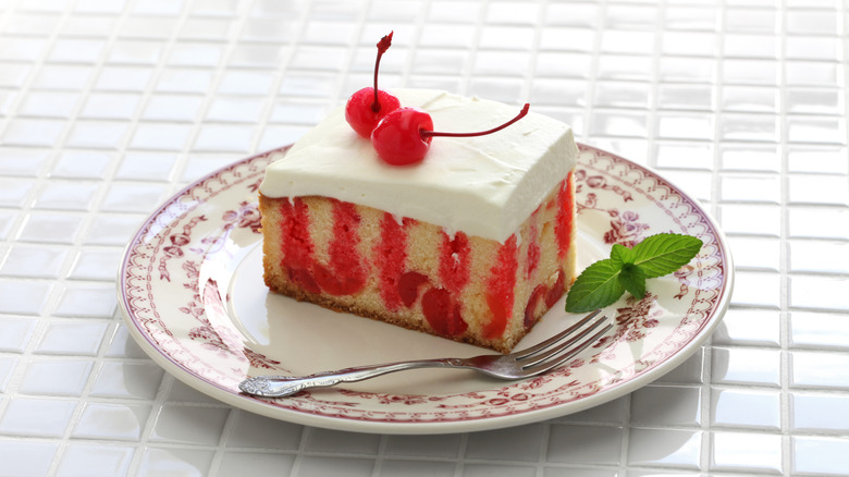 slice of Jello poke cake topped with two cherries on a plate with a fork and sprig of mint on the side