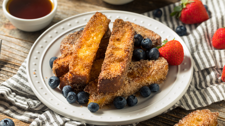 A plate of French toast sticks with blueberries and strawberries
