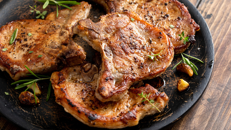 Closeup of a dark plate of cooked pork chops with rosemary garnish