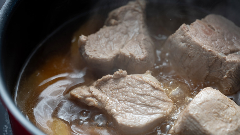 Four ribs boil in a pot of brown liquid.