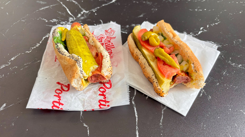 Two Chicago-style hot dogs with bites taken on parchment wrappers