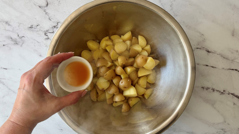 Hand holding small bowl of vinegar over bowl of chopped potatoes