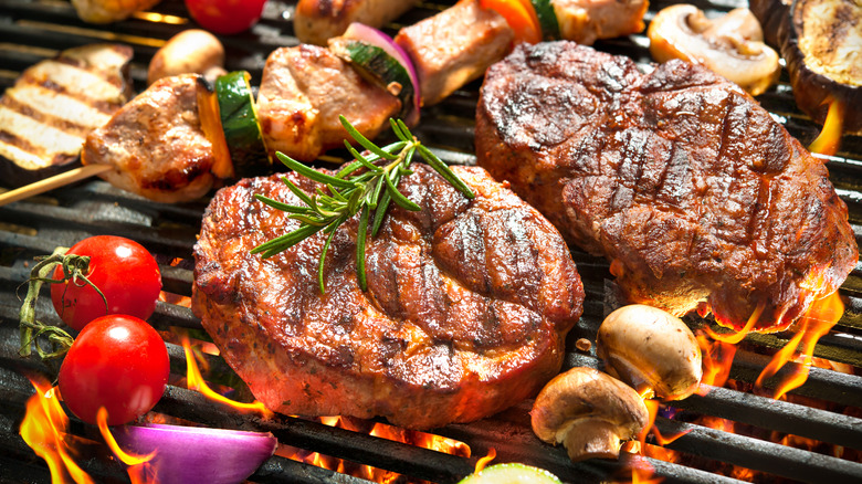 Steaks, sausages, and assorted skewered veggies on a hot, flaming grill