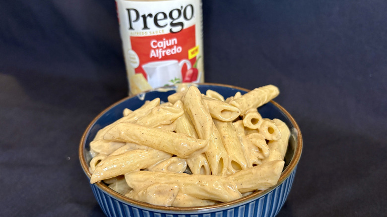 Saucy pasta in a bowl with a Prego Cajun Alfredo sauce jar behind it