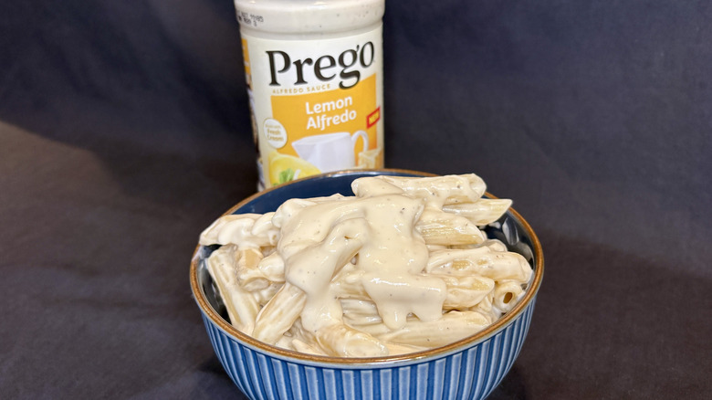 Creamy pasta in a bowl with a Prego Lemon Alfredo sauce jar behind it