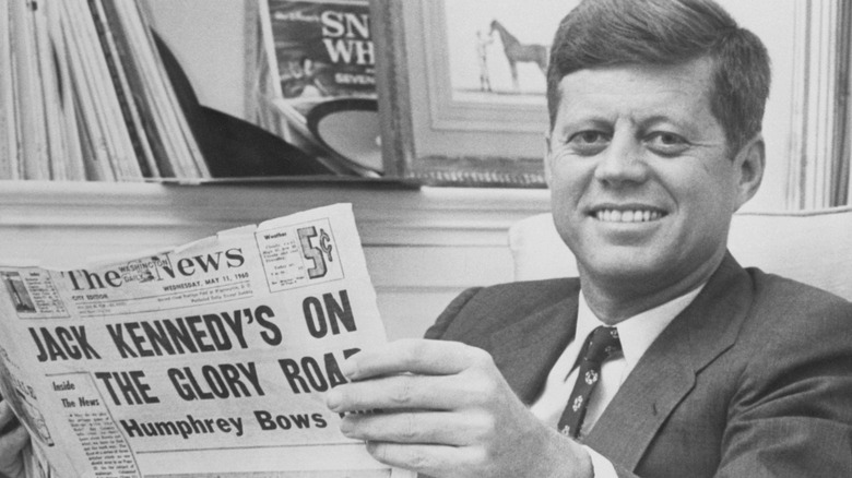 John F. Kennedy reading the newspaper and smiling