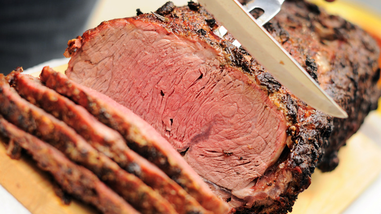 Knife slicing prime rib on wooden cutting board.