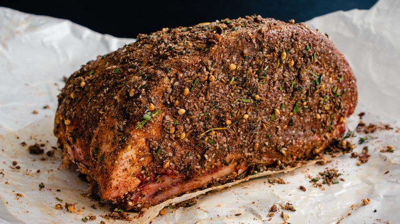 Raw prime rib covered in seasoning on parchment paper.