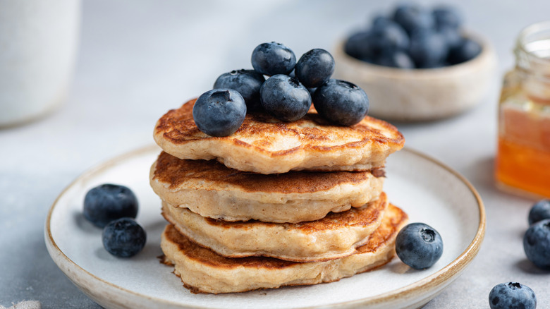 A plate stacked with pancakes topped with large blueberries