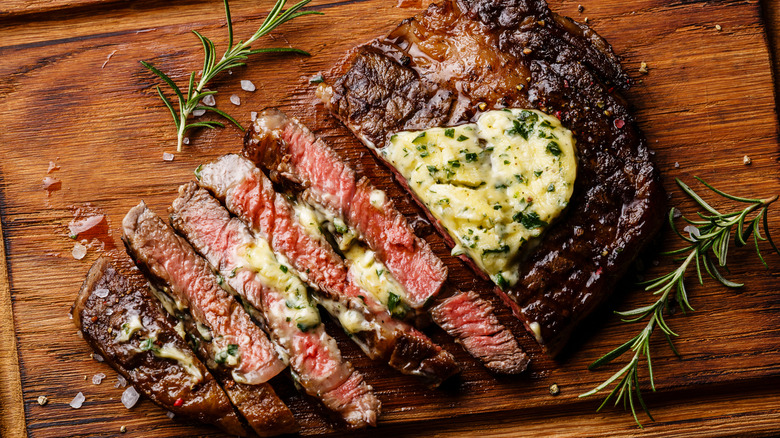 A steak cooked medium-rare with herb butter and fresh rosemary, sliced for serving on a wooden board.