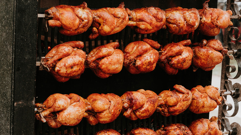 Four racks of rotisserie chickens being cooked