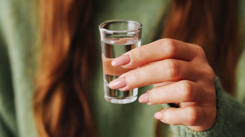 Person holding shot glass of clear liquid