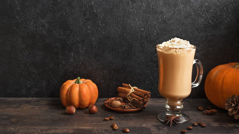 pumpkin spice latte with whipped cream on black background, pumpkin and spices around the glass for decor