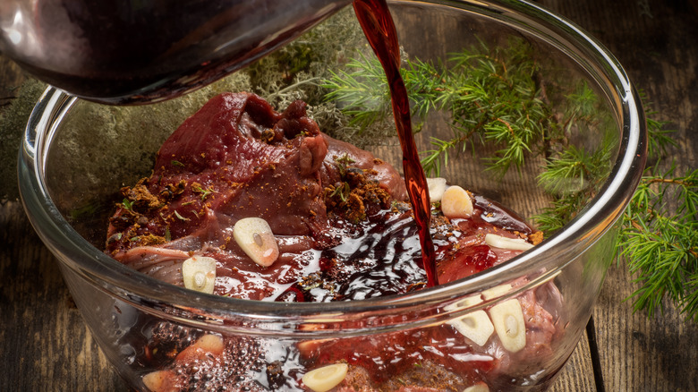 Red wine pouring on meat with spices and garlic