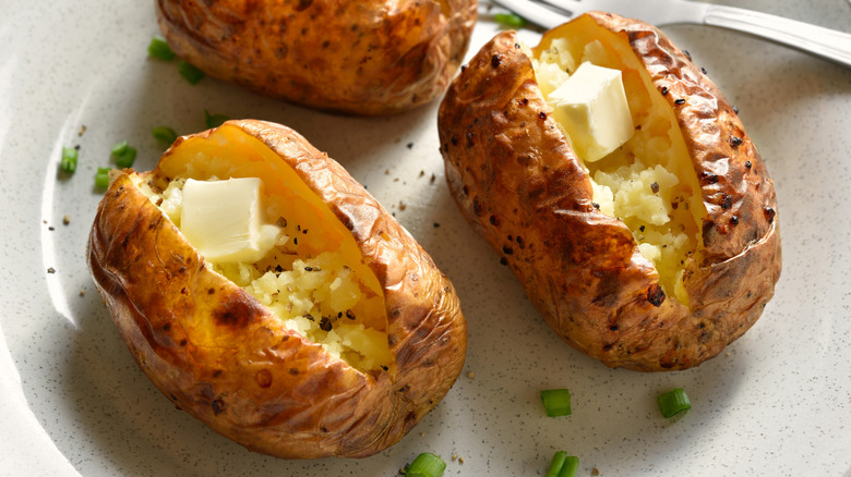 Three baked potatoes with butter on plate.