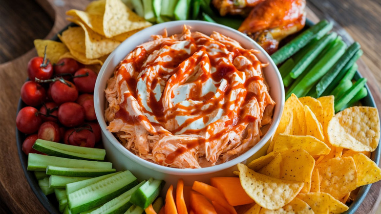 Platter of chips, wings, and vegetables around bowl of Buffalo chicken dip.