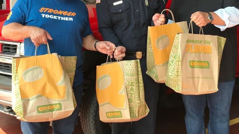 People holding brown Qdoba bags