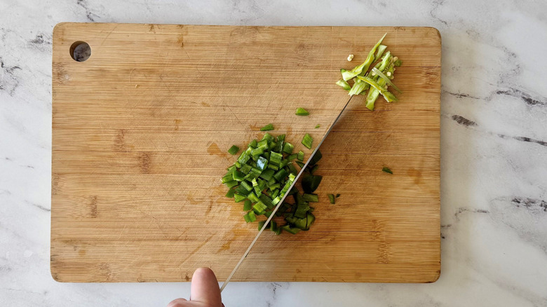 Knife cutting jalapeño on wooden board