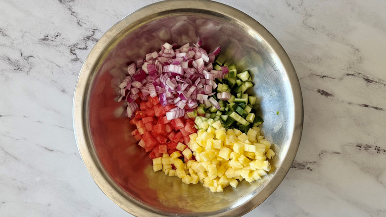 Diced watermelon, pineapple, red onion, and cucumber in bowl